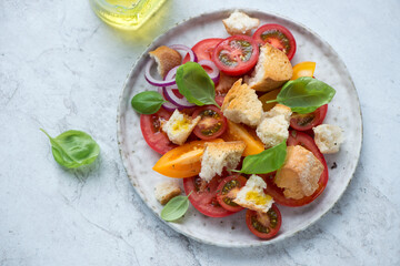 Panzanella or traditional italian tomato and bread salad on a white stone background, horizontal shot, elevated view