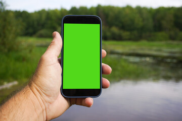 Hand  holding smartphone with green screen in front of river. cellular communication and wireless technologies away from the city concept.