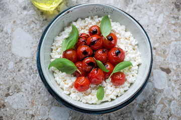 Caprese with cottage cheese, roasted cherry tomatoes and fresh basil, horizontal shot on a brown granite background, elevated view