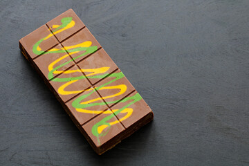 Milk Dubai chocolate bar decorated with green and yellow swirls lying on dark grey surface