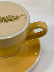 Bright yellow cup of latte coffee with crushed pistachio crumbs on top