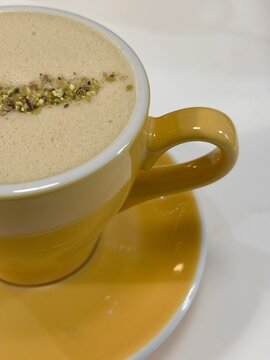 Bright yellow cup of latte coffee with crushed pistachio crumbs on top