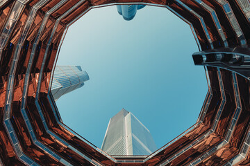 Symmetrical upward view from inside The Vessel, looking at its futuristic honeycomb structure against a blue sky in Hudson Yards, NYC.