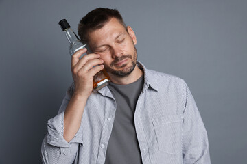 Naklejka premium Man with bottle of whiskey suffering from hangover on grey background
