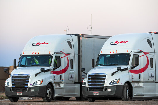 Two Ryder semi-trailer trucks parked side by side with branded cabs and trailers, representing commercial freight transport, logistics services, and long-haul trucking operations in the supply chain