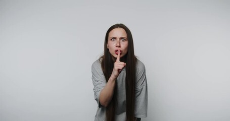 woman gestures for silence with her finger against her lips, expressing a request for quietness on white background