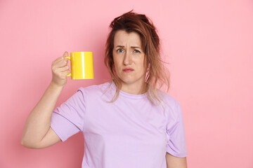 Woman with cup of coffee suffering from hangover on pink background