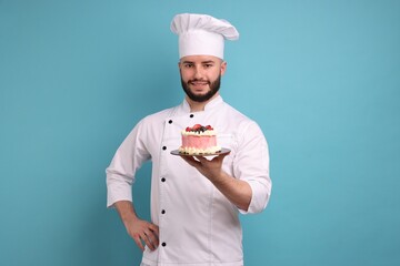 Happy confectioner in uniform holding cake with berries on light blue background