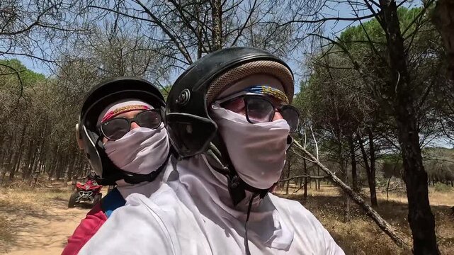 A selfie of couple riding an all-terrain vehicle (ATV) along a sandy road surrounded by trees in Tunisia. Adventure, travel, and nature exploration in North Africa.
