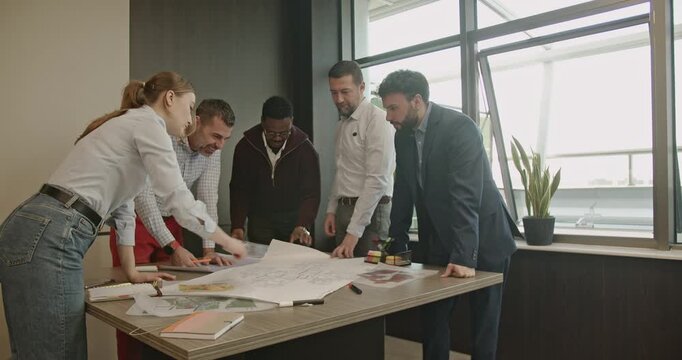 A diverse team of business professionals collaborates on a project, reviewing blueprints and engaging in teamwork.