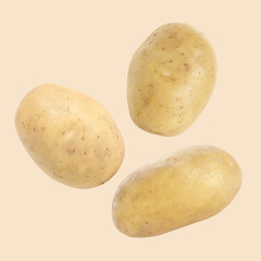 Three raw potatoes flying against beige background