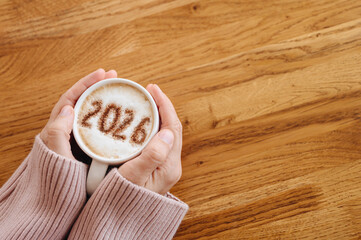 woman in cozy warm sweater enjoying hot coffee. On milk foam numbers 2026. New Year concept