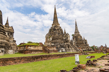 Fototapeta premium Ancient stupas of Wat Phra Si Sanphet in Ayutthaya Historical Park, Thailand under cloudy sky with visible ruins and grassy foreground