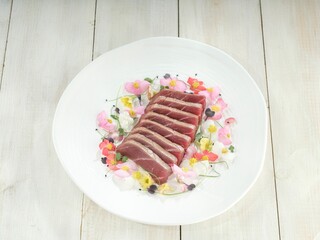 A row of precisely cut, seared tuna loin pieces rests among edible flowers, creating a delightful arrangement that is both visually appealing and flavorful