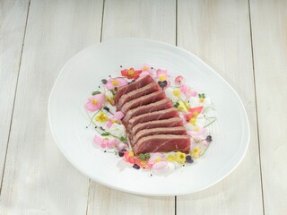 A carefully crafted plate features thinly sliced tuna, seared to perfection, arranged with edible flowers and delicate garnishes, against a clean white background
