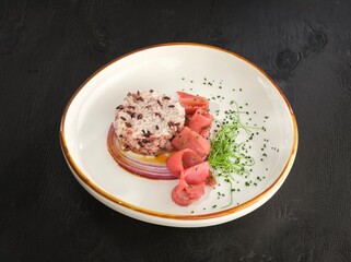 A delicately plated dish presents a vibrant blend of black rice, thinly sliced red onion, vibrant pink tuna, and fresh microgreens, creating a visual and gastronomic delight
