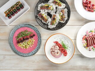 Prepared raw tuna dishes are arranged on various decorative plates. Garnishes of microgreens and edible flowers add visual appeal to the culinary creations on a white table