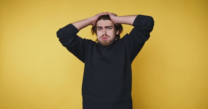 young man expresses frustration by holding his head, capturing a relatable moment of stress on yellow background