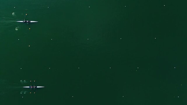 Top Shot View Of Rowers. National team precise movements slice through the water In beautiful  weather condition. Rowers paddling on the lake near the forest. The Athletes Training Routine.