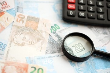 Brazilian reais banknotes and calculator with magnifying glass. Brazil real money, calc with loupe