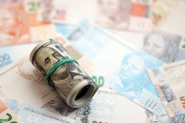 Roll of US dollar bills lies on big amount of Brazilian reais banknotes close up