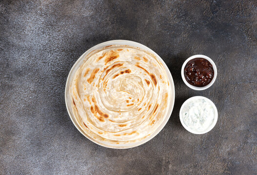 Indian flatbread paratha with raita sauce and chutney on gray background, top view. Indian food.