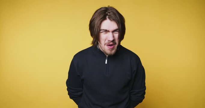 young man grimaces playfully on yellow background, showing a humorous expression that evokes laughter