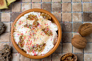 Autumnal dessert with walnuts, figs, and whipped cream, served in a rustic bowl. Seasonal dessert with colorful sprinkles on a ceramic tile background