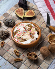 Autumnal dessert with walnuts, figs, and whipped cream, served in a rustic bowl. Seasonal dessert with colorful sprinkles on a ceramic tile background