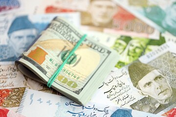 Stack of US dollar bills lies on big amount of Pakistan rupees banknotes close up