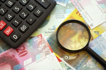 Swiss franc banknotes and calculator with magnifying glass. The current francs money bills and calc
