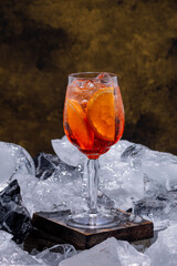 Aperol Spritz cocktail with orange slices and ice cubes in a wine glass, served on a wooden block with crushed ice. Refreshing summer drink, perfect for bars, menus, and lifestyle use.