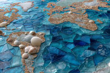An oceanic map formed by shards of blue glass with seashells marking coastal borders and coral pieces designating islands.