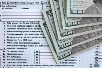 Big amount of United States dollar bills on table with 1040 tax return form
