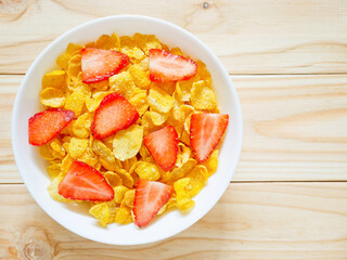 Golden cornflakes cereal with strawberries on wooden background