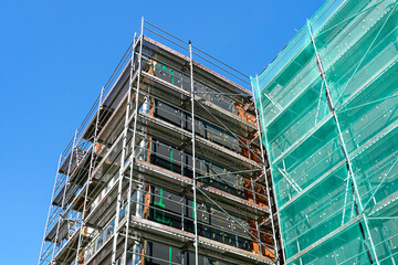 Building Facade Renovation with Metal Scaffolding and Green Safety Netting Against Blue Sky