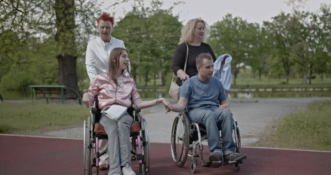 A happy couple in wheelchairs holding hands, enjoying a day in the park with their supportive caregivers. This video highlights companionship, disability inclusion, and outdoor activities.