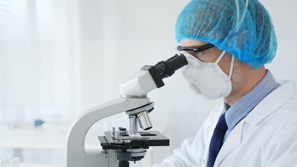 Experienced scientist examining microscopic sample, wearing full protective gear inside sterile research laboratory. Health care and science concept