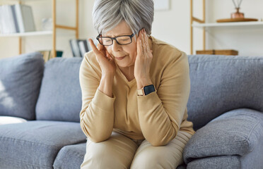 Obraz premium Tired frustrated old senior woman touching head, feeling headache, migraine, sitting on couch alone depressed after loss, grief, trauma, nervous breakdown, physical, mental or emotional problems