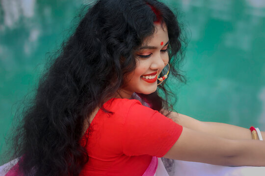 Retro style portrait of a beautiful Indian Bengali woman in red and white traditional ethnic saree and jewellery and sindoor in outdoor lighting. Indian culture, religion and fashion
