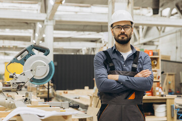 Carpenter wearing protective gear posing in workshop with crossed arms