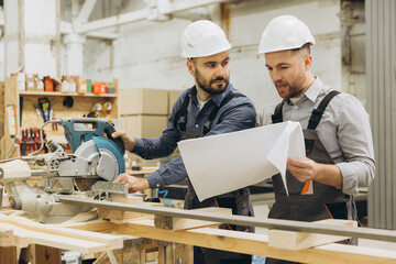 Carpenters discussing blueprint and using circular saw in workshop