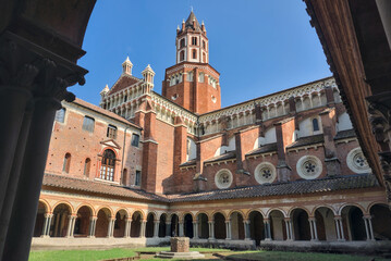 Vercelli, Italy: The historic cloister of the Basilica di Sant'Andrea, with its Romanesque and Gothic architecture, framed by a bell tower against a blue sky.