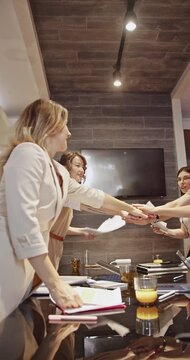 Happy business workers celebrates a major achievement in their modern office. They stack hands, throw papers in the air, clap, and high-five, demonstrating successful collaboration and teamwork.