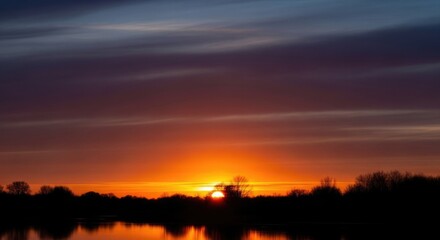 Dramatic Sunset Over Silhouetted Landscape and Water