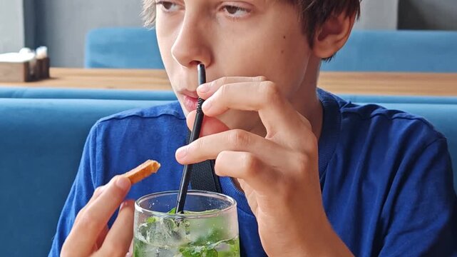 Close-up of a teenage boy drinking a sugary soda and eating fast food French fries. Young Caucasian guy is sitting in a fast food restaurant - and drinking a cold drink using a plastic tube