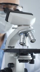 Scientist wearing lab coat and protective glasses using a modern microscope in a laboratory setting, conducting research and experiments in a scientific environment. Health care and science concept