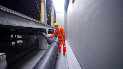 Worker inspects large pipe installation in narrow industrial corridor during daytime