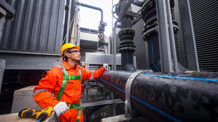 Worker in orange safety gear inspecting industrial pipes in a power plant