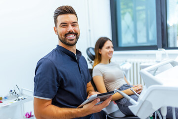 Obraz premium Male Dentist Posing with Tablet and Female Patient in Background